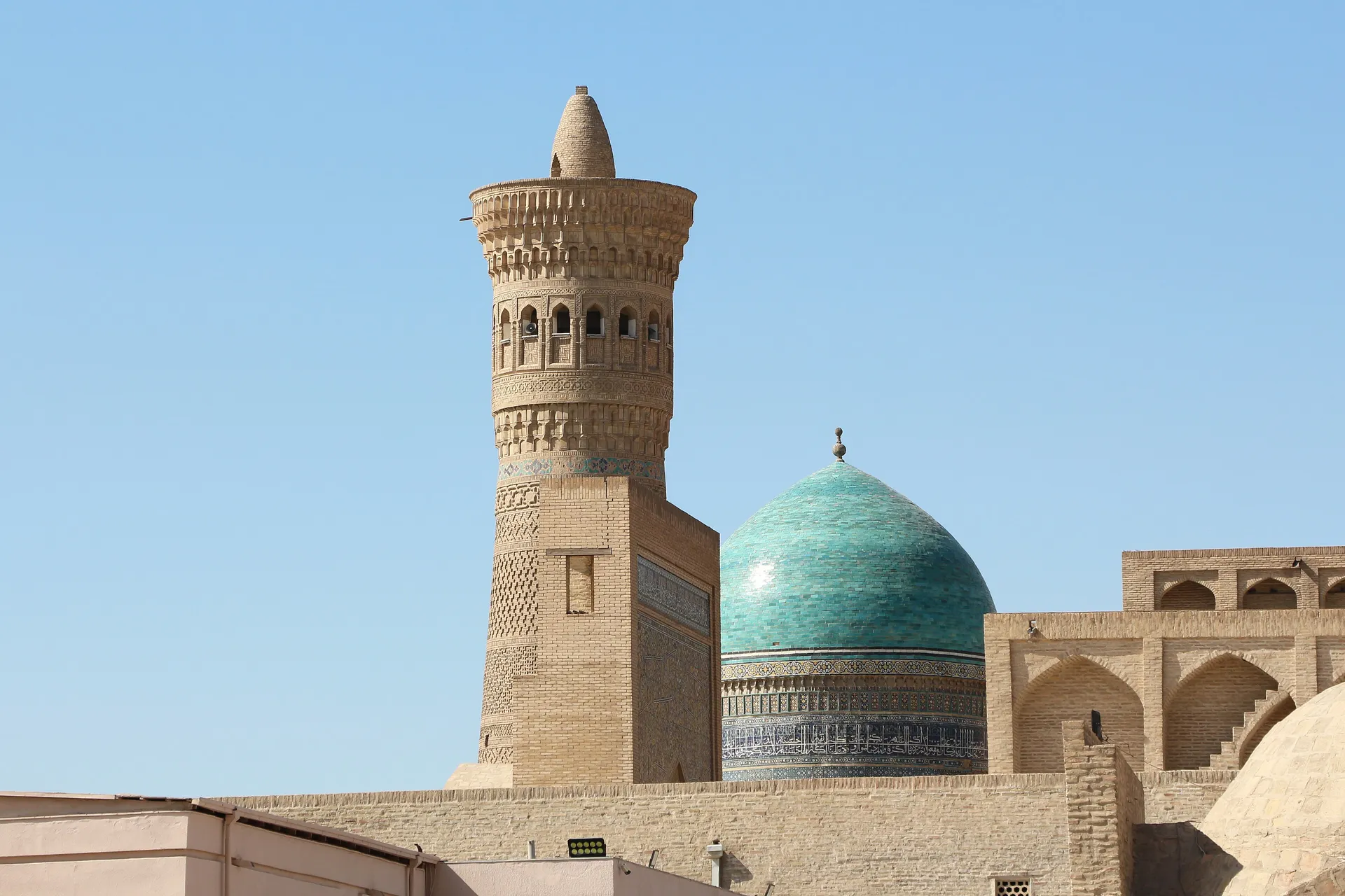 The Kalyan Minaret of 1127 beside the turquoise dome of the Mir-i-Arab madrasah — the heart of old Bukhara.