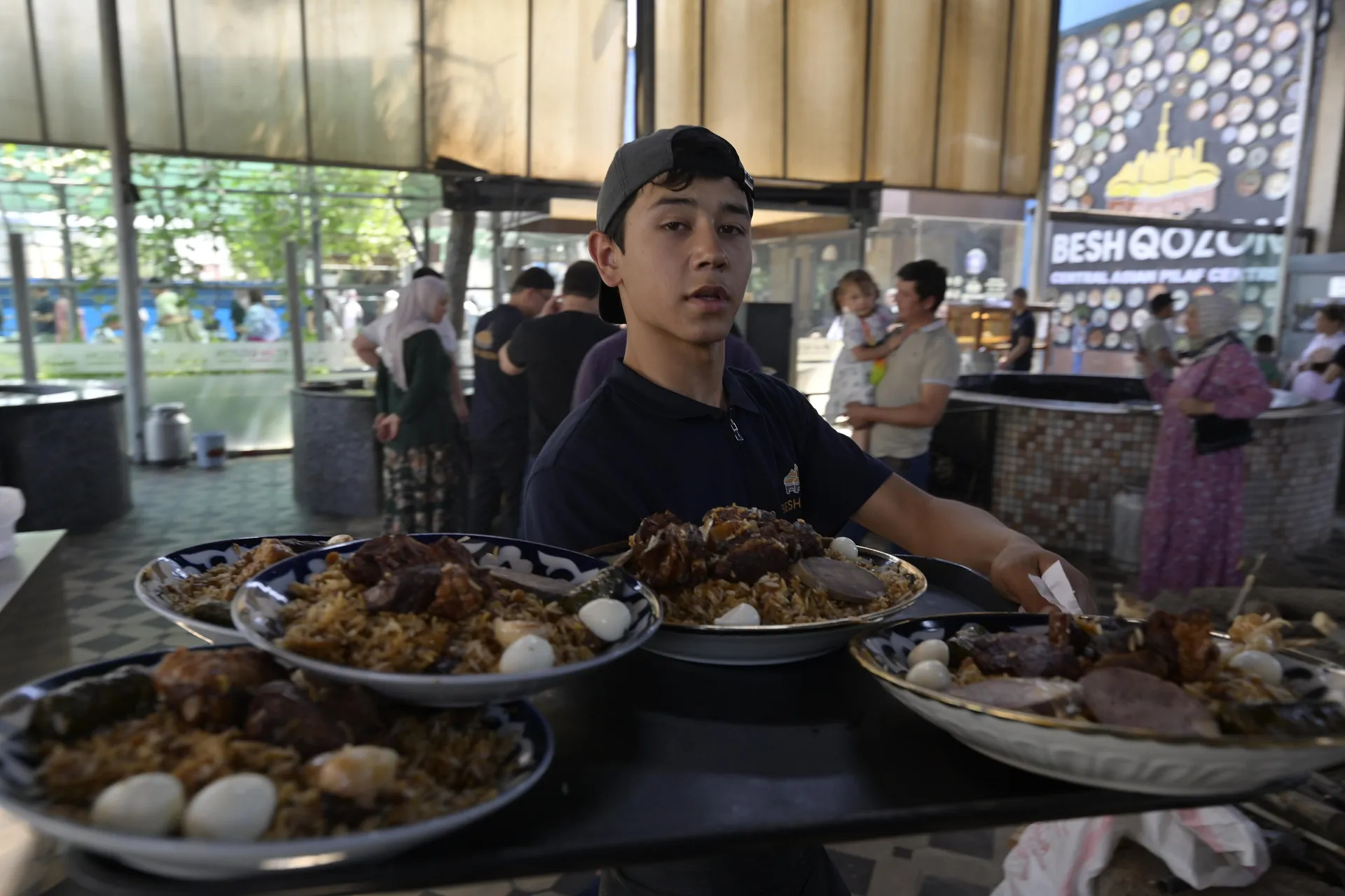 A young server carrying plates of plov through a busy plov centre, where the day's rice is cooked in giant kazans from dawn.