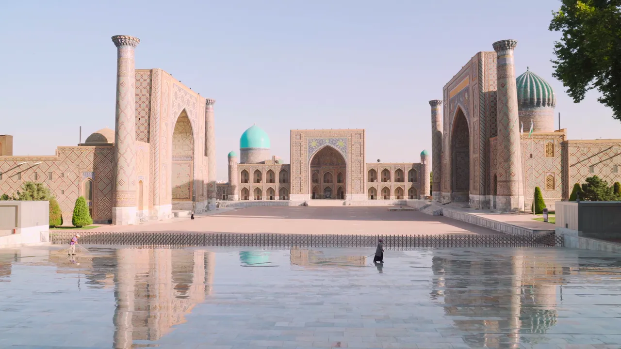 Morning light on the three madrasahs of the Registan, their portals reflected in the wet paving of the square.