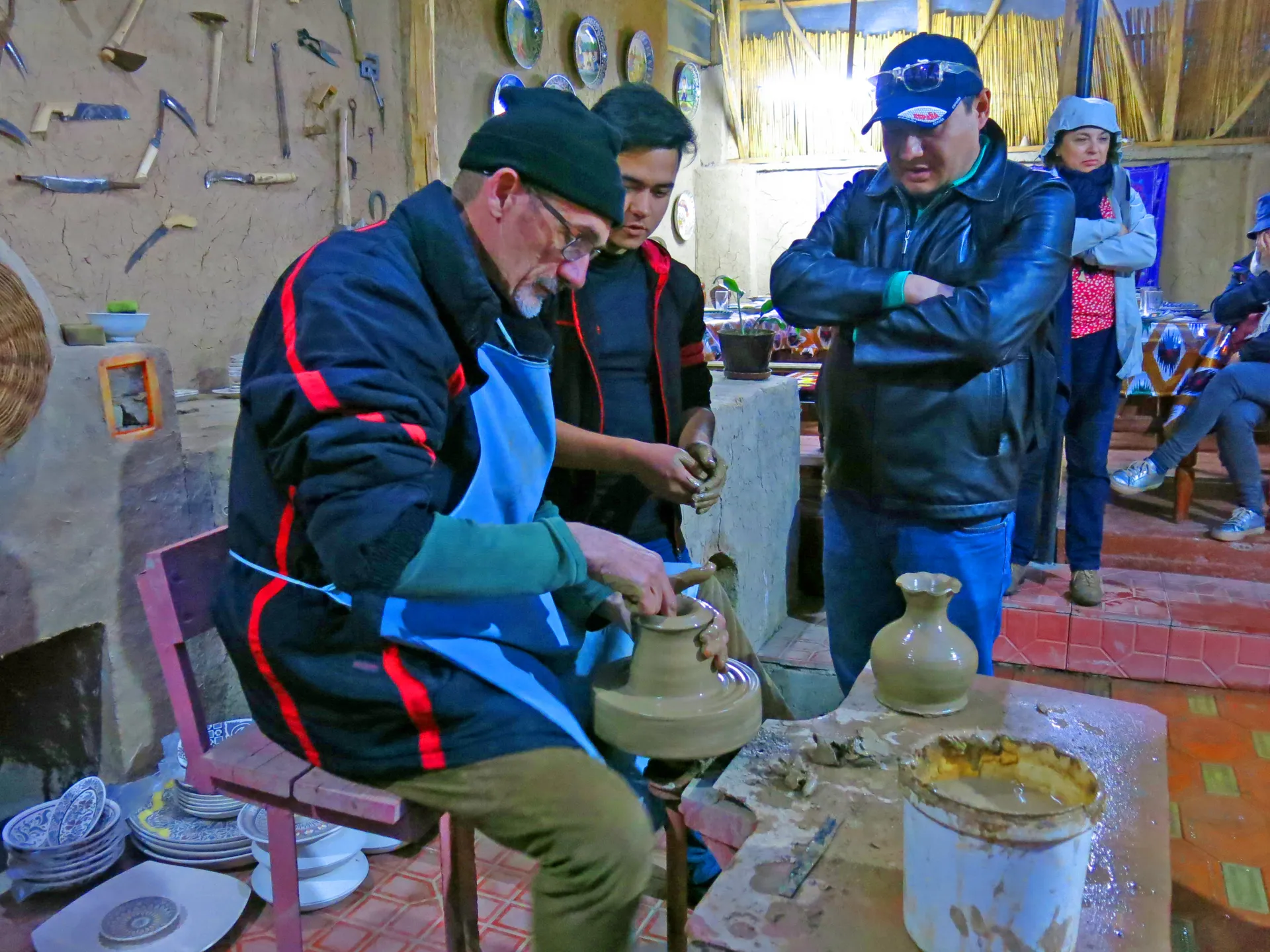 A master potter shapes a vessel at the wheel while visitors watch, in one of Rishtan's family workshops.