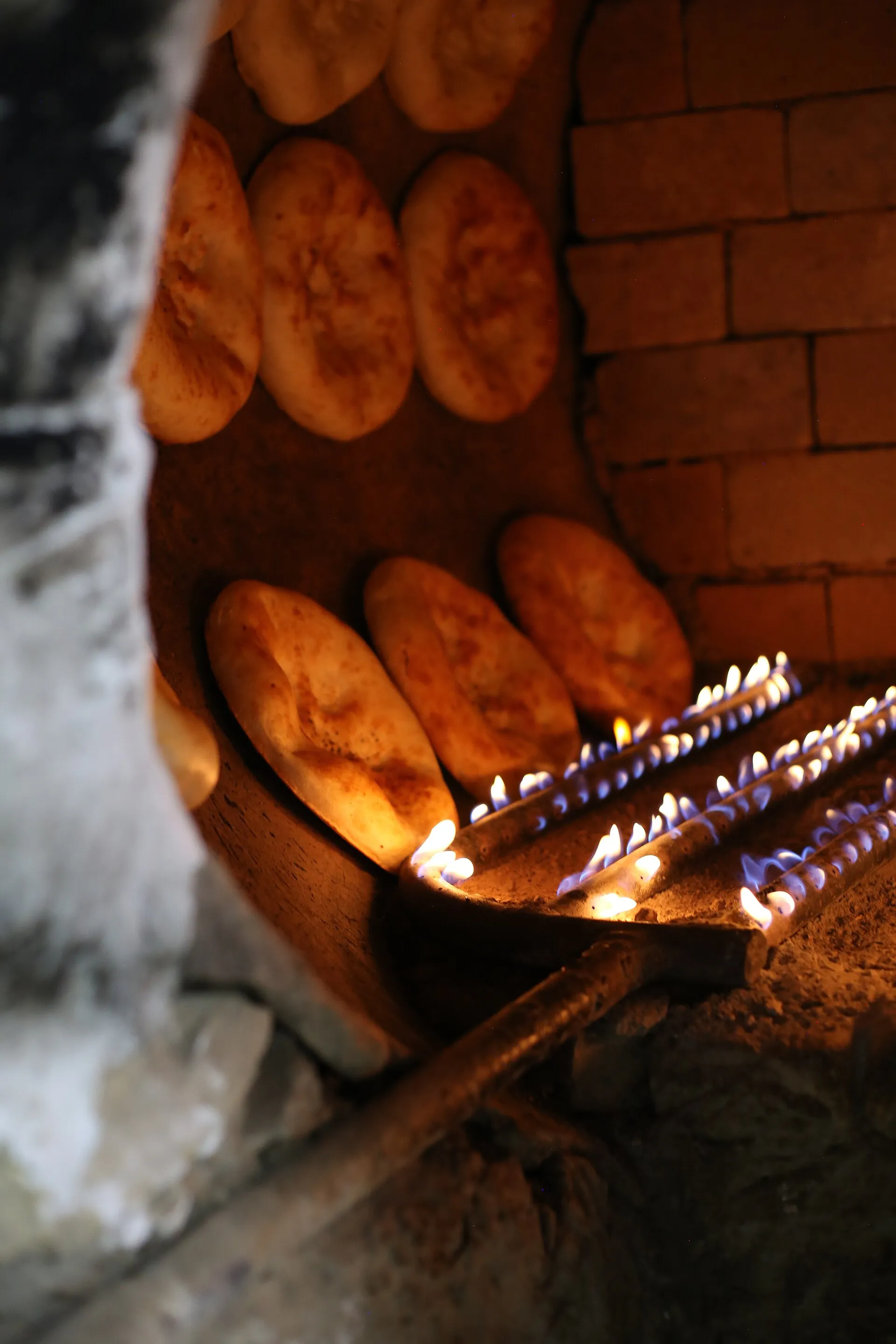 Rounds of dough baking on the hot inner wall of a clay tandir, lit by the fire below.